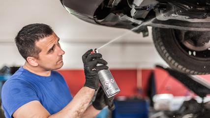 Car master mechanic repairer lubricates screws with machine cleaner spray