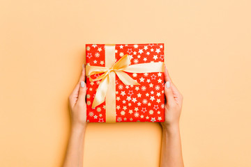 Flat lay of woman hands holding gift wrapped and decorated with bow on gold background with copy space. Christmas and holiday concept