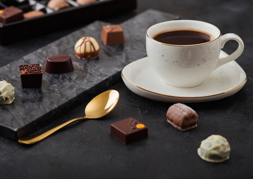 Luxury Chocolate candies selection with cup of black coffee and golden spoon on black marble board and dark table background.