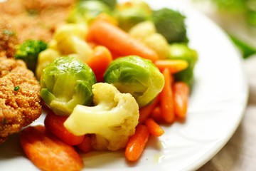 Chicken breast and vegetables. Baked chicken fillet, carrots, Brussels sprouts, broccoli, cauliflower. Food in a plate on a light wooden background. Close-up. Food on white plate 