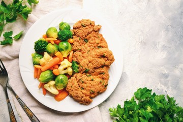 Chicken breast with vegetables. Baked chicken fillet, carrots, Brussels sprouts, broccoli, cauliflower. Food in a plate on a light wooden background.