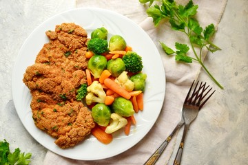Chicken breast with vegetables. Baked chicken fillet, carrots, Brussels sprouts, broccoli, cauliflower. Food in a plate on a light wooden background.