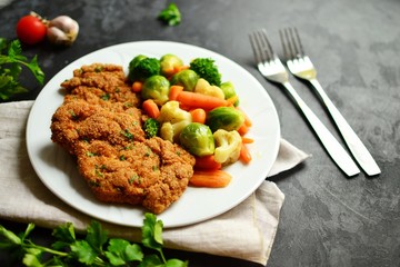 Chicken breast and vegetables. Grilled, baked chicken breast with carrots, brussels sprouts and broccoli. Meat in a white plate on a dark background isolated.
