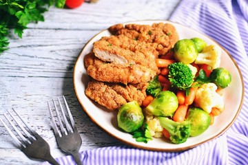 Chicken breast with vegetables. Baked chicken fillet, carrots, Brussels sprouts, broccoli, cauliflower. Food in a plate on a light wooden background.