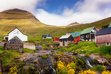 Fototapeta na wymiar Colorful houses of Funningur village with a small river and outstanding mountains on background. Faroe Islands, Denmark.