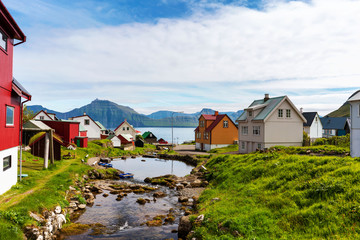 Fototapeta na wymiar Colorful houses of Gjogv village and a small river flows into fjord. Faroe Islands, Denmark.