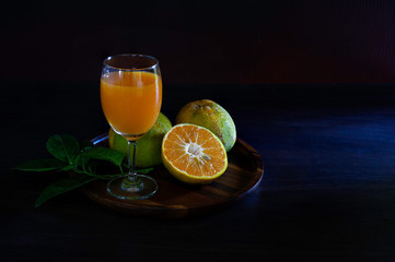Fresh oranges and orange juice in the brown wooden tray on dark background which has dim ligh