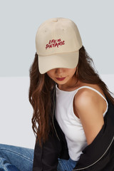 Cropped upward shot of a dark-haired girl, wearing beige baseball cap with print with lettering...