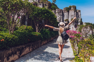 Beautiful excited blonde woman backpacker walks and admires tropical landscapes at paradise island hotel in Sanya, China. Luxury vacation resort concept banner. Asia travel lifestyle tourist back view