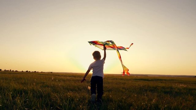 A boy runs across the field at sunset with a kite flying over his head. A chidhood dream. Kids Games