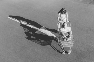 Black and white shot of Two happy hipster girls having fun with shopping cart outdoors