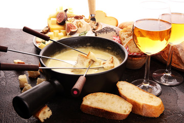Gourmet Swiss fondue dinner on a winter evening with assorted cheeses on a board alongside a heated pot of cheese fondue with two forks dipping