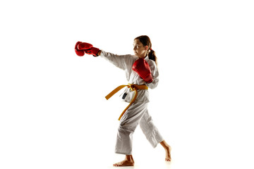 Fototapeta na wymiar Confident junior in kimono practicing hand-to-hand combat, martial arts. Young female fighter with yellow belt s training on white studio background. Concept of healthy lifestyle, sport, action.