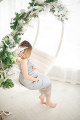 Beautiful pregnant woman in a bright interior under Christmas. Pregnant and Christmas decorations in the Scandinavian style. Woman on New Year's swing