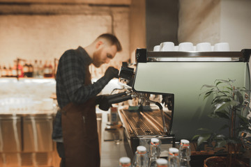 Bearded man barista steaming milk on a professional coffee machine. Process of cooking coffee on a...