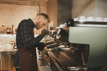 Portrait of a bearded man barista steaming milk on a professional coffee machine. Process of cooking coffee on a coffee machine in the coffee shop. Barista creating cappuccino in cafe