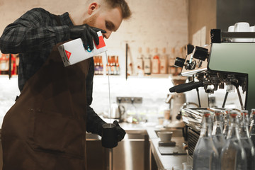 Young barista is pouring milk in a cup to prepare coffee drink in a coffee shop. Ambitious coffee...