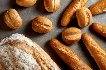 Fresh pastries. French baguettes, buns and wheat bread on a gray stone surface. Top view.