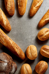 Fresh pastries. French baguettes, buns and rye bread on a gray stone surface. Top view.