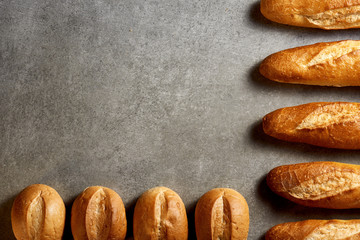 Fresh baguettes and buns on a gray stone surface. Top view.