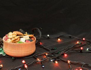 Healthy snacks in the wooden bowl together with Christmas fairy lights. Eat healthy food the whole yer. With black background. New Year mood.