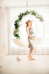 Beautiful pregnant woman in a bright interior under Christmas. Pregnant and Christmas decorations in the Scandinavian style. Woman on New Year's swing