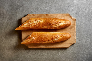 Two halves of baguette on a wooden board. Gray surface. Top view.