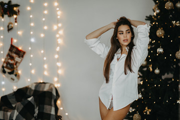 Young woman stands against the background of the Christmas tree and garlands.