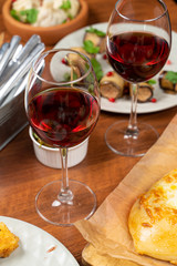 Two glasses of red wine with green olives on a table full of meals