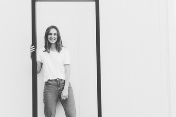 Black and white shot of young woman wearing white t-shirt and denim jeans is posing against the grey wall