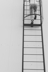 Black and white shot of Woman climbing ladder on a roof