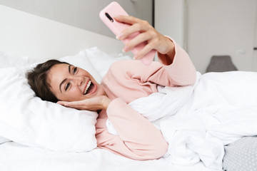 Cheerful lovely young girl wearing pajamas laying in bed