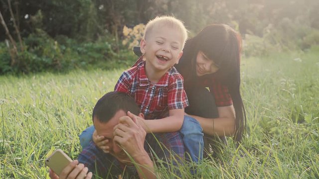 happy family teamwork outdoors have fun concept outdoors slow motion video. mom dad and son take a photo with a smartphone in nature are sitting on the grass have lifestyle fun playing .mom girl dad