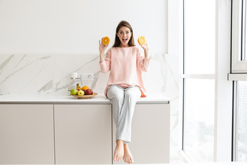 Cheerful lovely girl sitting on a kitchen desk with bowl of fruits