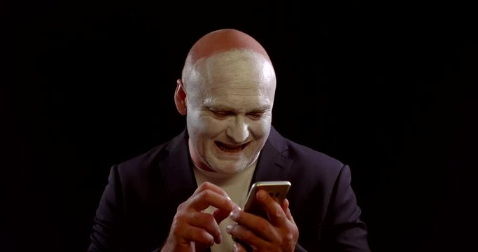 strange man with white makeup on face is laughing and using cell phone, touching sensor screen