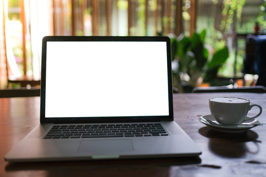 A cup of cappuccino coffee with laptop white screen on table. Royalty high quality free stock photo image of coffee cup with laptop for working in a coffee shop, typing with blank screen white color