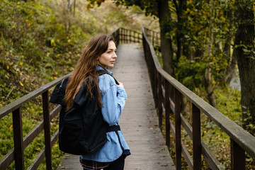 Woman tourist with a backpack walks on a bridge in the autumn forest.