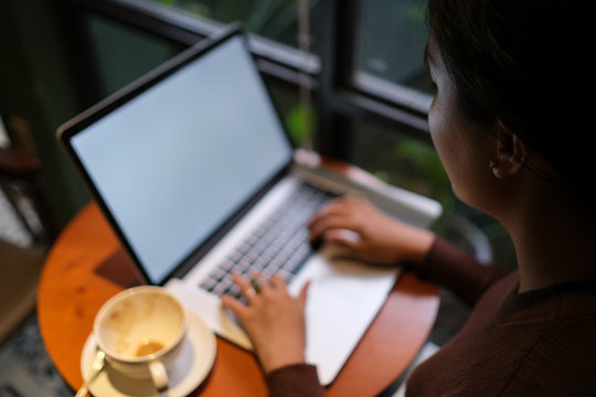 A young girl working with a cup of cappuccino coffee with laptop white screen on table. Royalty high quality free stock photo image of woman typing, working on laptop with a coffee cup in coffee shop