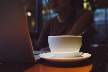 A young girl working with a cup of cappuccino coffee with laptop white screen on table. Royalty high quality free stock photo image of woman typing, working on laptop with a coffee cup in coffee shop