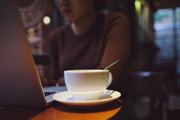 A young girl working with a cup of cappuccino coffee with laptop white screen on table. Royalty high quality free stock photo image of woman typing, working on laptop with a coffee cup in coffee shop