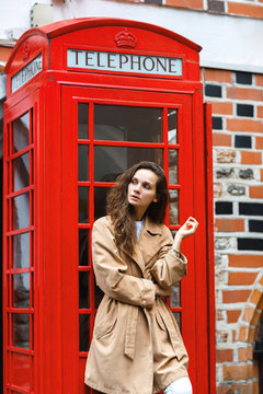 A young brunette woman stands near a red telephone box in London