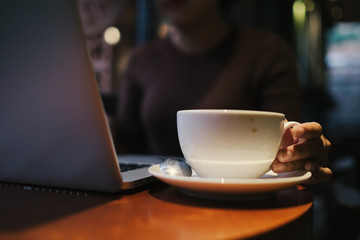 A young girl working with a cup of cappuccino coffee with laptop white screen on table. Royalty high quality free stock photo image of woman typing, working on laptop with a coffee cup in coffee shop