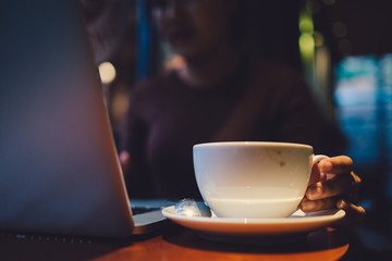 A young girl working with a cup of cappuccino coffee with laptop white screen on table. Royalty high quality free stock photo image of woman typing, working on laptop with a coffee cup in coffee shop