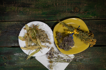 On a green plate are two bouquets of dried medicinal herbs - from oregano and St. John's wort. On a...