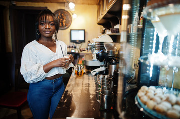 Stylish african american women in white blouse and blue jeans posed at cafe with caramel latte.
