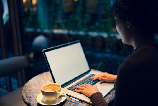 A young girl working with a cup of cappuccino coffee with laptop white screen on table. Royalty high quality free stock photo image of woman typing, working on laptop with a coffee cup in coffee shop
