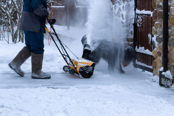 Man clears snow with a snow blower  in house yard. Snowblower in working. Snowy winter yard.