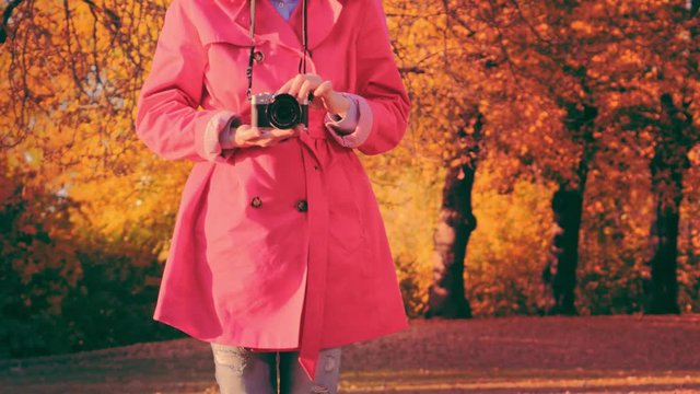Fashionable woman with camera in park in autumn. Trendy young woman in Red cloak