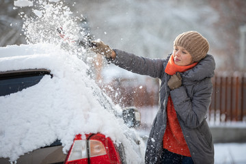 Pretty, young woman cleaning her car from snow after heavy snowstorm (color toned image)