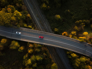 Winding road in autumn forest at sunset in mountains. Aerial view. Top view of beautiful asphalt roadway and orange trees. Highway through the woodland in fall. Trip in europe. Travel and nature